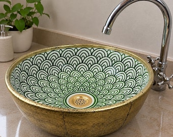 May include: A round vessel sink featuring a white interior with a green scalloped fan pattern and a gold-toned exterior. The sink includes a gold-colored drain assembly and is paired with a polished chrome gooseneck faucet fixture.