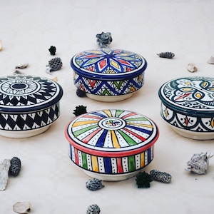 Peut inclure: Quatre contenants de rangement ronds en céramique avec couvercles. Chaque contenant présente un motif géométrique coloré différent. Les contenants sont sur une surface blanche.