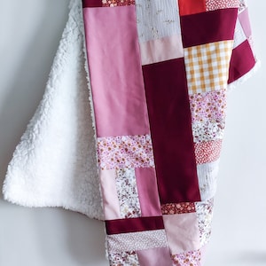 Peut inclure: Une courtepointe patchwork avec une variété de motifs floraux et géométriques dans des tons de rose, bordeaux et or. La courtepointe est faite de tissus doux et est parfaite pour se blottir sur le canapé.