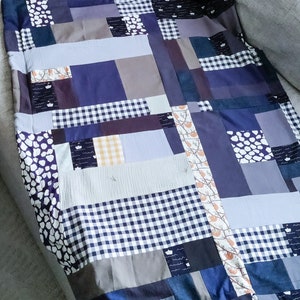 Może przedstawiać: Kołdra patchworkowa wykonana z r&oacute;żnych odcieni niebieskiego, szarego i białego. Kołdra składa się z kwadrat&oacute;w i prostokąt&oacute;w o r&oacute;żnych rozmiarach i wzorach, w tym kraty, kropek i wzoru kwiatowego.