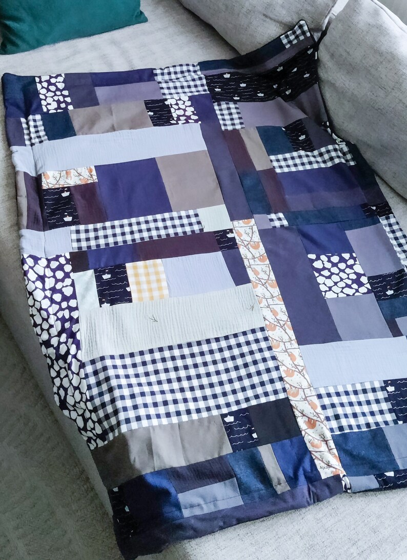 Może przedstawiać: Kołdra patchworkowa wykonana z r&oacute;żnych odcieni niebieskiego, szarego i białego. Kołdra składa się z kwadrat&oacute;w i prostokąt&oacute;w o r&oacute;żnych rozmiarach i wzorach, w tym kraty, kropek i wzoru kwiatowego.