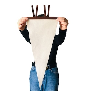 May include: A person is holding up a large, white triangular banner with brown fabric trim at the top. The banner is blank and ready for customisation.