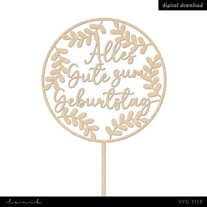 Puede incluir: Un adorno para pastel de madera con un diseño circular con un borde de hojas y el texto "Alles Gute zum Geburtstag".