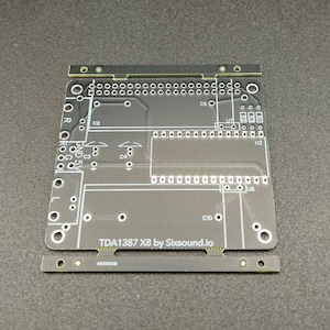 Könnte beinhalten: Eine schwarze Leiterplatte mit dem Text "TDA1387 X8 by Sixsound.io" darauf gedruckt. Die Platine hat mehrere Komponenten, darunter Kondensatoren, Widerstände und integrierte Schaltungen.