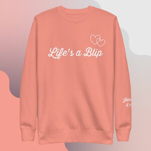 May include: A coral pink sweatshirt with the text "Life's a Blip" in white cursive font. Two white hearts are above the text. The text "Jam 4-4" is on the right sleeve.