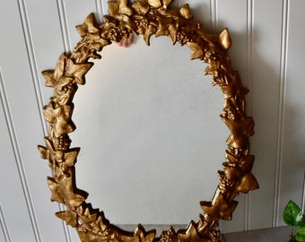Espejo ovalado vintage de hierro fundido dorado con diseño de hojas de hiedra y bayas.