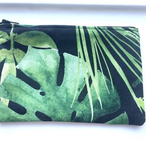 May include: A black zippered pouch with a tropical leaf print. The print features large green leaves on a black background.