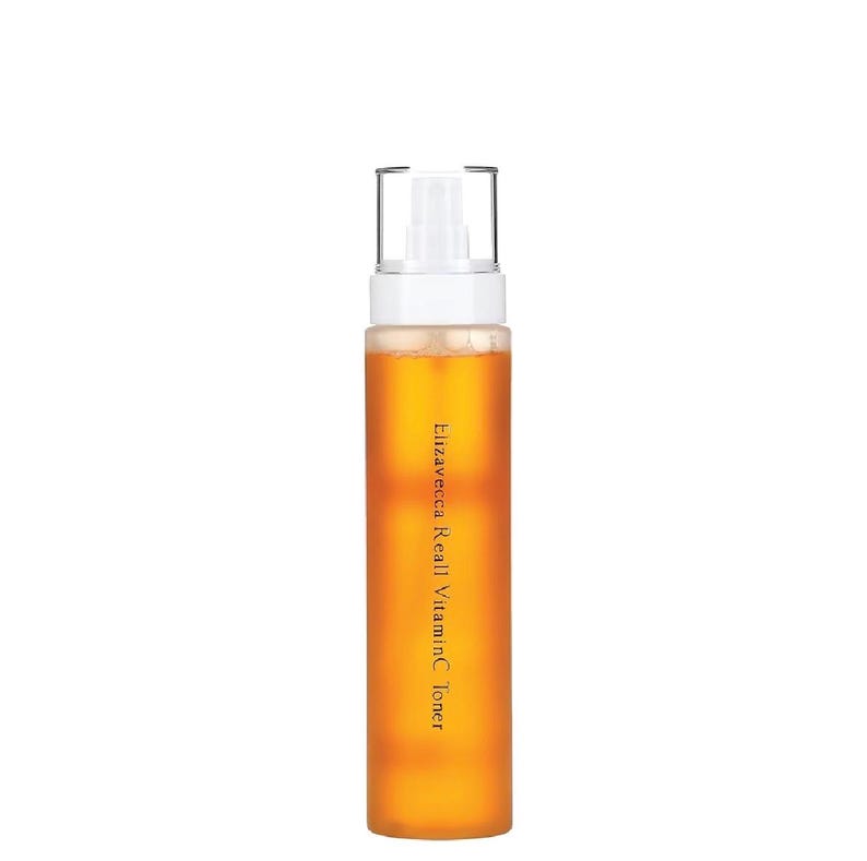 Puede incluir: Una botella transparente de t&oacute;nico Elizavecca Real Vitamin C. La botella contiene un l&iacute;quido de color dorado y tiene un pulverizador blanco. El texto "Elizavecca Real VitaminC Toner" est&aacute; impreso verticalmente en la botella.