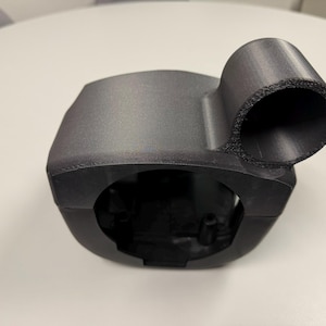 May include: A black 3D printed plastic steering wheel adapter with a round opening on the side.