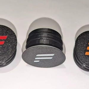 May include: Three phone grips with different colored logos. The logos are a red "F", a white "F", and an orange "F".