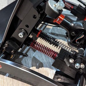 May include: Close-up of a black racing simulator pedal set with red springs and a black metal frame.