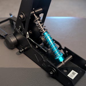 May include: A black mechanical component with a blue spring and silver coil. The device has a complex design with multiple parts and is likely part of a larger machine or system. The component is set against a gray background.