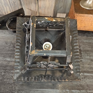 May include: A black metal ceiling light fixture with a square base and a decorative design. The light fixture has a single bulb socket and a clear glass bulb.