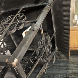 May include: A black metal lantern with a square shape and intricate scrollwork details. The lantern has a hinged top and a decorative design.