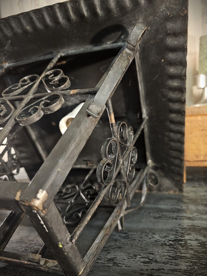 May include: A black metal lantern with a square shape and intricate scrollwork details. The lantern has a hinged top and a decorative design.