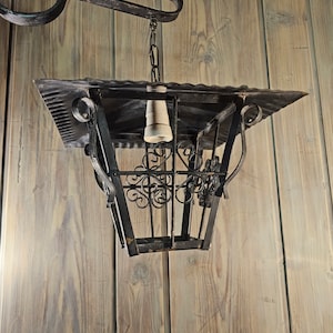 May include: A black metal lantern with a decorative design hangs from a chain attached to a hook on a wooden wall.