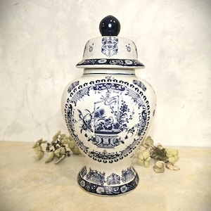 May include: A white and blue ceramic ginger jar with a lid. The jar features intricate blue floral and decorative patterns. The lid is topped with a dark blue sphere. The jar is a decorative home accent.