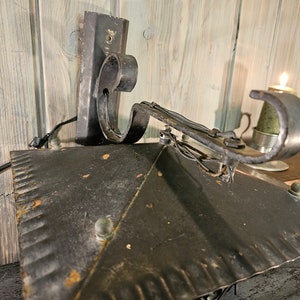 May include: Black metal wall sconce with a decorative scroll arm and a textured metal shade. The sconce is mounted on a wooden wall.