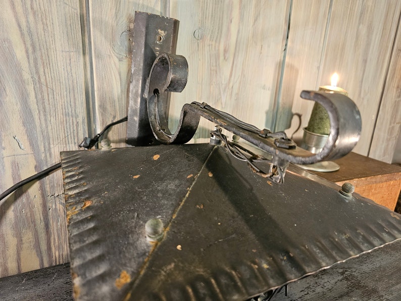 May include: Black metal wall sconce with a decorative scroll arm and a textured metal shade. The sconce is mounted on a wooden wall.