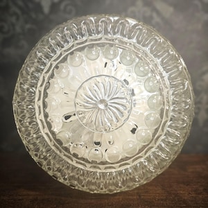 May include: A clear glass ceiling light fitting with a decorative, textured design. The fitting has a round shape and a central dome with a floral pattern.