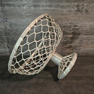 May include: A silver wire fruit bowl with a circular base and a wide, open top. The bowl is made of a delicate wire mesh.