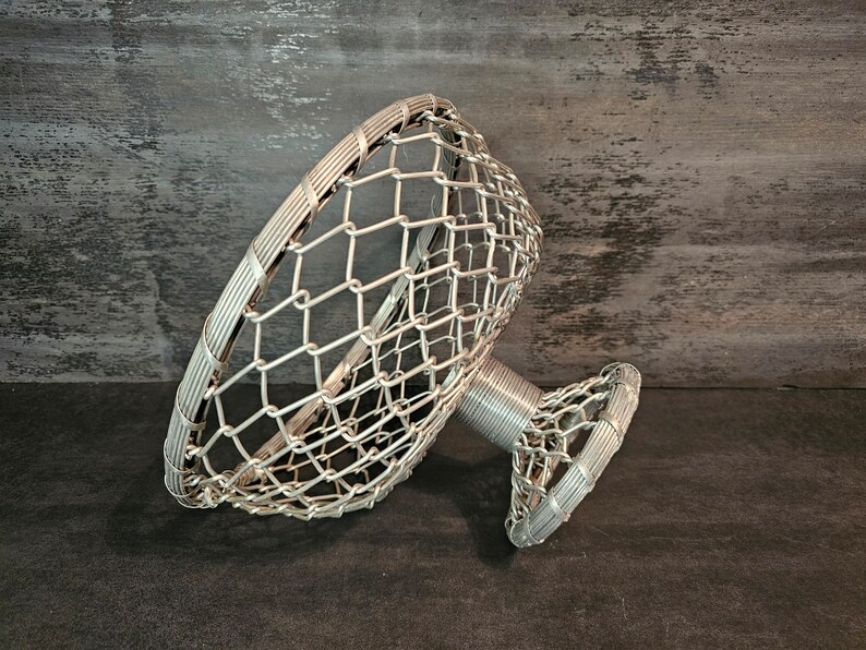 May include: A silver wire fruit bowl with a circular base and a wide, open top. The bowl is made of a delicate wire mesh.