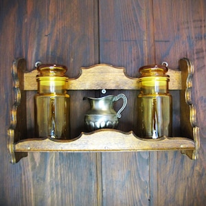 May include: A wooden spice rack with two amber glass jars and a silver pitcher on a dark wood background.