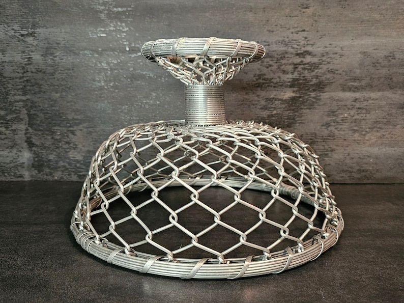 May include: A silver wire mesh dome-shaped bowl with a wire base. The bowl is made of woven wire and has a circular shape.