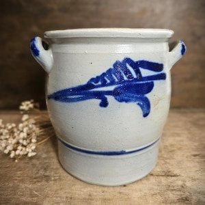 Könnte beinhalten: Ein kleiner weißer Keramiktopf mit blauen bemalten Designs. Der Topf hat zwei Henkel und einen blauen Streifen um die Basis.