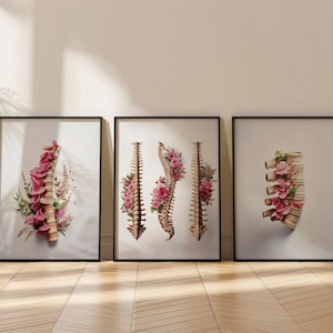 May include: Three framed art prints featuring watercolor illustrations of human spines adorned with pink flowers. The artwork is set against a white background, with black frames. The prints are displayed on a light-colored wooden floor.
