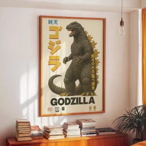 Op de afbeelding: Een ingelijste vintage Godzilla-poster. De poster toont een gedetailleerde illustratie van Godzilla in een dreigende pose, met Japanse tekst en de titel "GODZILLA" in vette letters. Het kleurenpalet omvat tinten groen, geel en bruin.