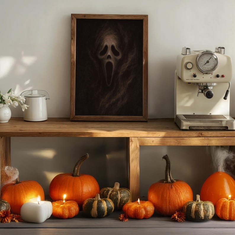 May include: A wooden framed print of the Scream mask hangs above a wooden shelf. The shelf displays a coffee machine, pumpkins, candles, and a white teapot. The pumpkins are orange and green, and the candles are lit.