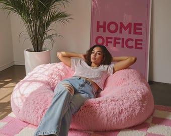 May include: A large, pink, fluffy beanbag chair. The chair is in a room with a pink and white checkered rug and a poster that says "HOME OFFICE". A large potted plant is in the background.