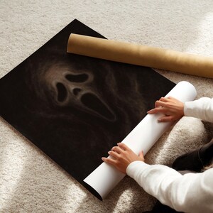 May include: A black poster featuring the iconic Scream mask design. The poster is rolled up with a white paper roll and a brown cardboard tube. The image is on a light-colored carpet.