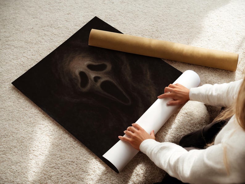 May include: A black poster featuring the iconic Scream mask design. The poster is rolled up with a white paper roll and a brown cardboard tube. The image is on a light-colored carpet.