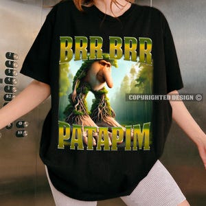May include: Black t-shirt featuring a green, yellow and brown graphic of a creature with a long nose and the text "BRR BRR PATAPIM".