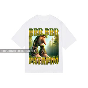 May include: White t-shirt featuring a green and yellow graphic of a creature with a long nose and the text "BRR BRR PATAPIM".