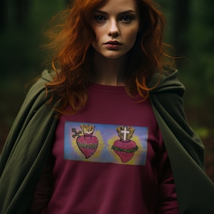 May include: A maroon sweatshirt with a graphic of two sacred hearts. The hearts are surrounded by thorns and flames. The graphic is on a blue background.