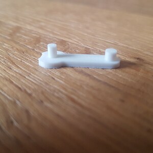May include: White plastic bone-shaped object with two small round protrusions on the top.