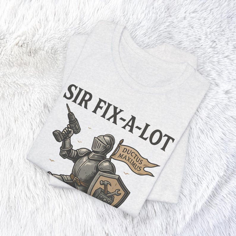 Peut inclure: T-shirt gris clair avec le texte "SIR FIX-A-LOT" au-dessus d'une illustration d'un chevalier tenant une perceuse. Le chevalier a un bouclier avec des outils et une banni&egrave;re qui dit "DUCTUS MAXIMUS".