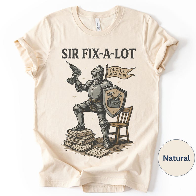 Peut inclure: T-shirt de couleur naturelle avec un dessin d'un chevalier tenant une perceuse, un bouclier et une banni&egrave;re avec l'inscription "DUCTUS MAXIMUS". Le texte "SIR FIX-A-LOT" est au-dessus du chevalier. Une petite chaise en bois est &agrave; droite.