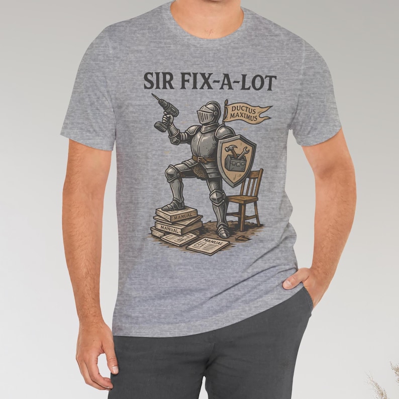Peut inclure: T-shirt gris clair avec l'inscription "SIR FIX-A-LOT" au-dessus d'une illustration d'un chevalier en armure tenant une perceuse. Le chevalier est debout sur des manuels, avec un bouclier et une banni&egrave;re "DUCTUS MAXIMUS".