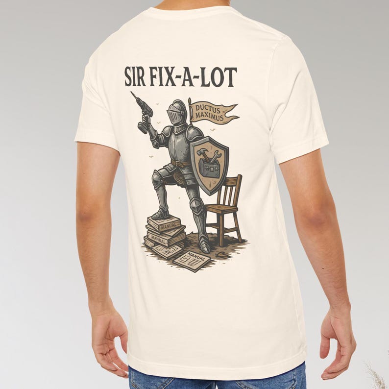 Peut inclure: T-shirt cr&egrave;me avec un chevalier de dessin anim&eacute; tenant une perceuse et un bouclier, avec le texte "SIR FIX-A-LOT". Le chevalier est debout sur des manuels, avec une petite chaise en bois. La banni&egrave;re dit "DUCTUS MAXIMUS".