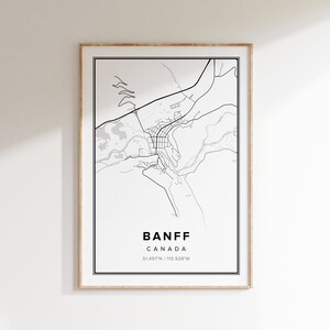 Peut inclure: Une carte en noir et blanc de Banff, Canada, réalisée en lignes. La carte montre les rues de la ville, les rivières et les montagnes environnantes. Le texte "BANFF CANADA 51.497°N / 115.928°W" est imprimé sous la carte.