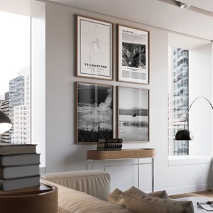 May include: A modern living room with a white wall featuring four framed black and white prints. The prints are of a map of Yellowstone National Park, a waterfall, a geyser, and a lake. A black floor lamp with a white shade is in the corner of the room. A white sofa with brown cushions is in the foreground.
