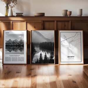 Pode incluir: Três impressões emolduradas em preto e branco de Banff, Canadá. Uma apresenta uma cordilheira refletida na água, outra um rio através de uma floresta e a terceira um mapa da cidade. As impressões são exibidas em um armário de madeira.
