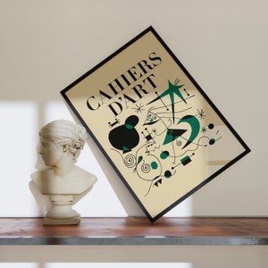 May include: A black framed poster with a beige background and the text "CAHIERS D'ART" in black. The poster features an abstract design with black and green shapes and lines.