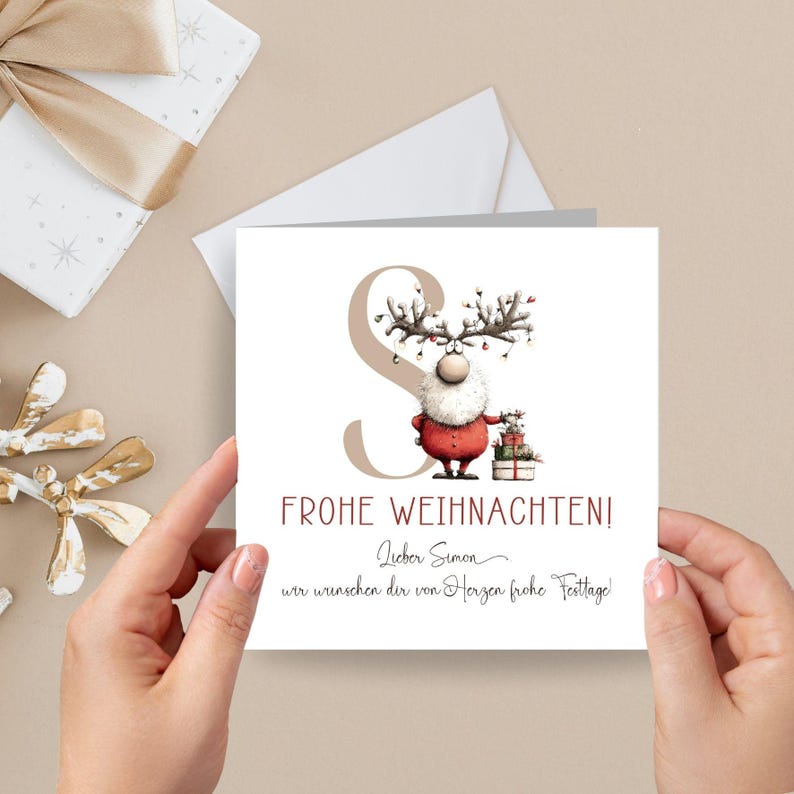 Pu&ograve; includere: Biglietto di Natale con un personaggio renna in abito rosso, con regali. Il biglietto presenta il testo "FROHE WEIHNACHTEN!" e un messaggio scritto a mano. Lo sfondo &egrave; beige chiaro.