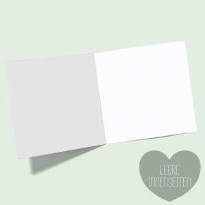 Pu&ograve; includere: Un biglietto di auguri aperto con pagine bianche vuote, su uno sfondo verde chiaro. Una forma di cuore grigia con il testo "LEERE INNENSEITEN" si trova nell'angolo in basso a destra.