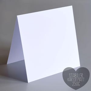 Pu&ograve; includere: Un biglietto bianco piegato, in piedi su uno sfondo grigio. Il biglietto &egrave; realizzato in carta opaca spessa. Una grafica a forma di cuore grigio nell'angolo in basso a destra contiene il testo "STABILER KARTON MATT 250G".